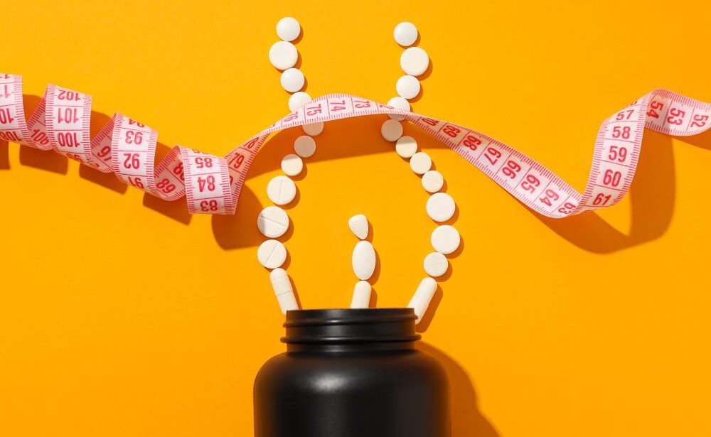 A black bottle with white tablets arranged as a person and a measuring tape on an orange background, highlighting weight management products or diet supplements.