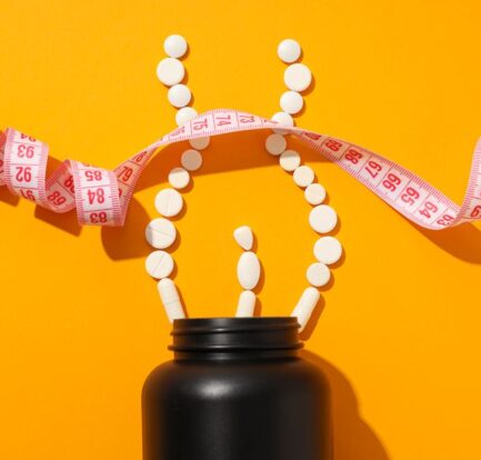 A black bottle with white tablets arranged as a person and a measuring tape on an orange background, highlighting weight management products or diet supplements.