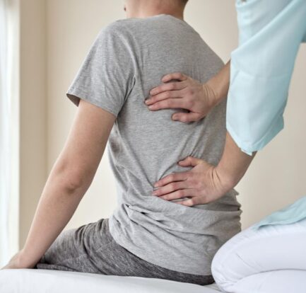 A person sits on an exam table while a chiropractor for slipped disk presses on their lower and middle back, possibly as part of a physical assessment.